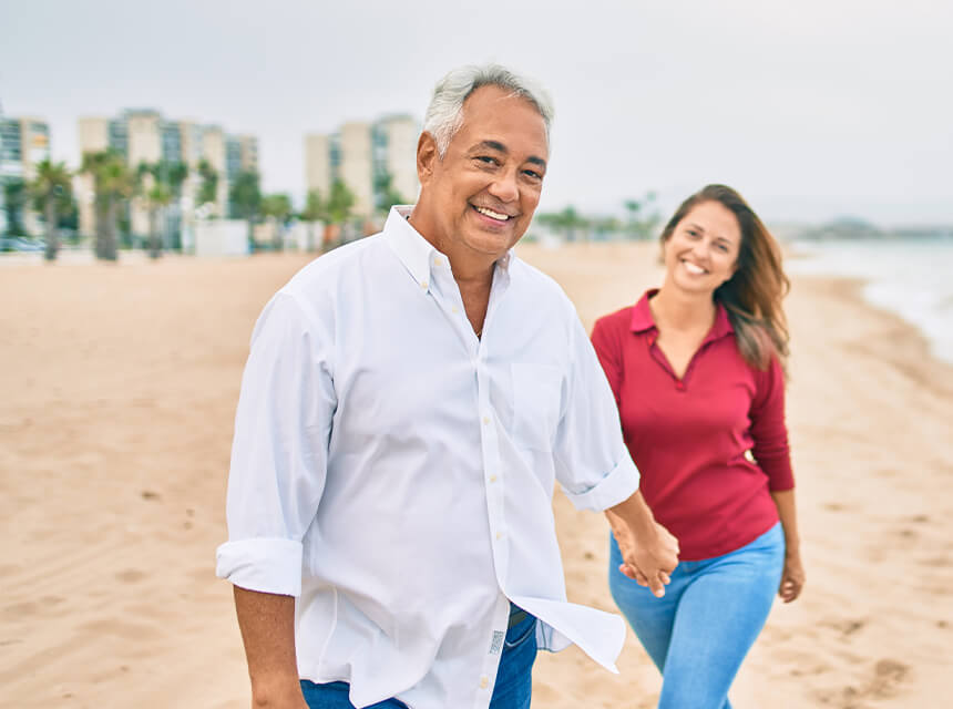 Couple smiling and holding hands while walking on the beach